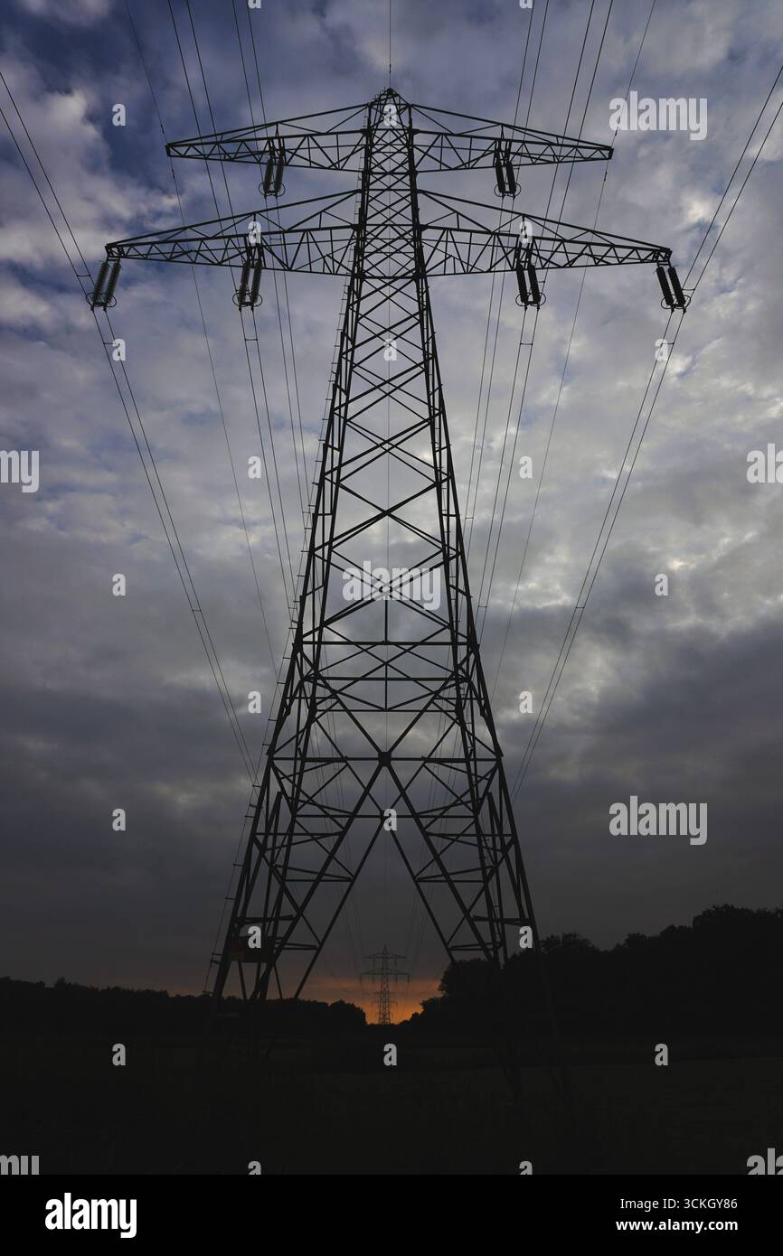 High-voltage transmission tower against a dramatic cloudy sky Stock Photo