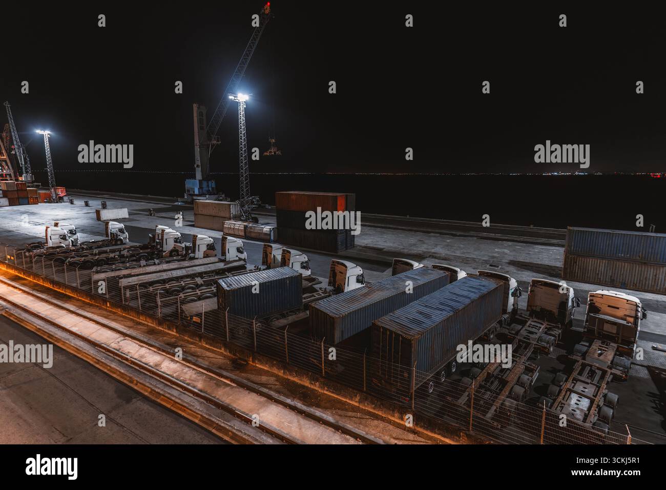 Industrial port at night with cargo trucks, shipping containers, and ...