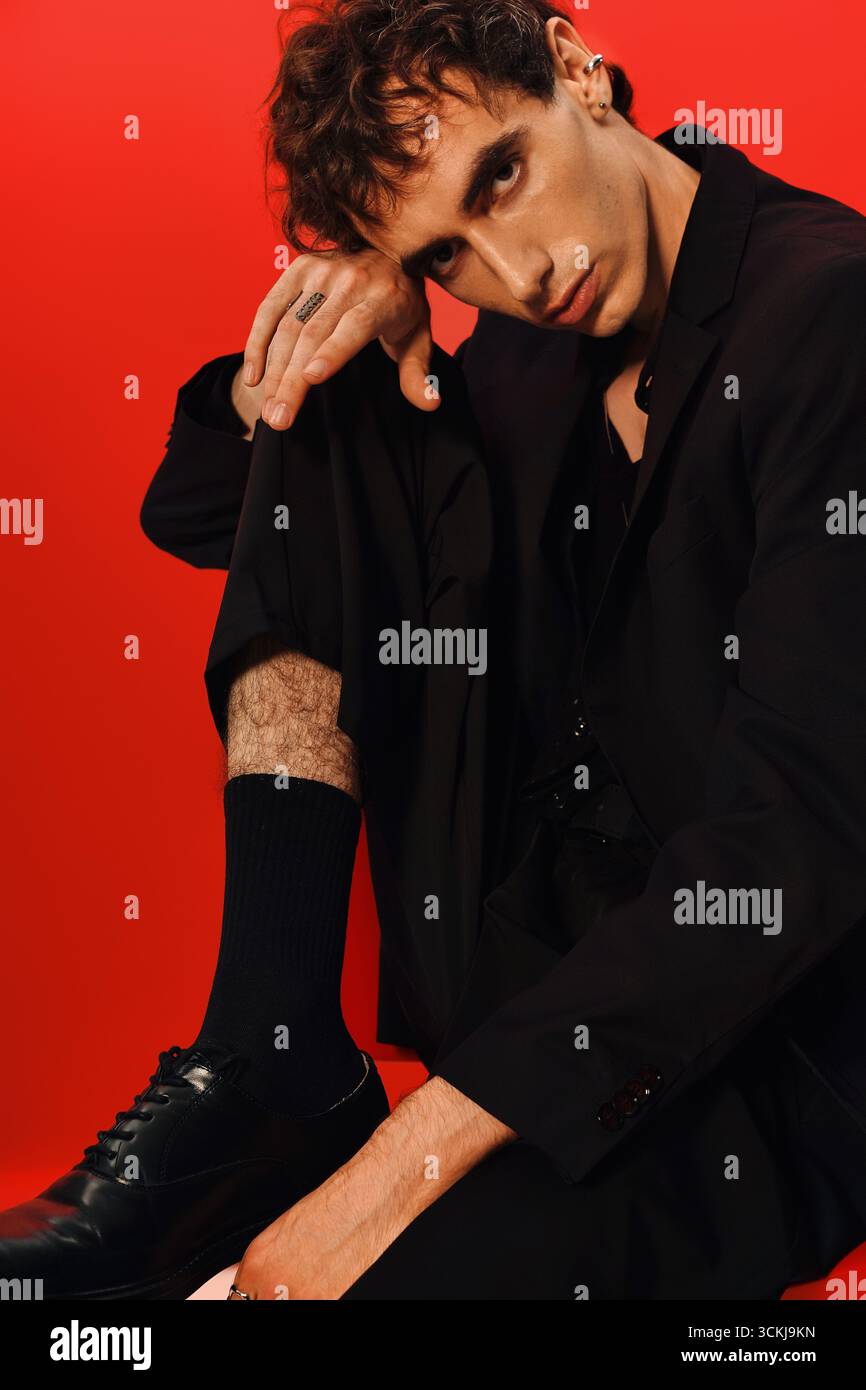 Stylish man in elegant attire poses confidently against a bold red ...