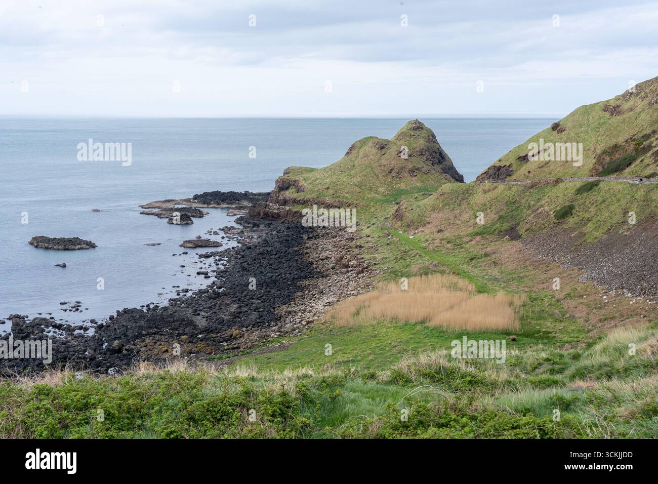 Daytime view of the Bay of the Cow in Northern Ireland, with calm waters, coastal cliffs, and a clear blue sky. Stock Photo
