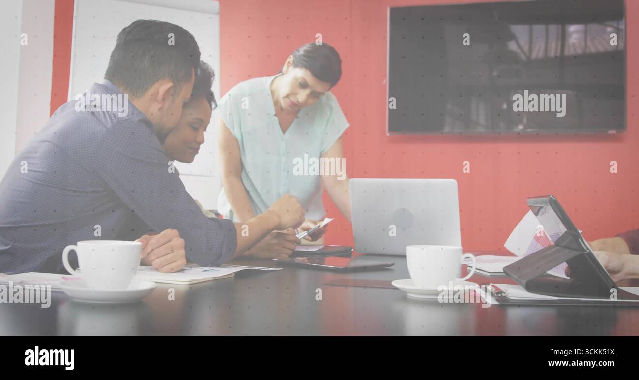 Collaborating professionals leaning over documents and devices at conference table, with coffee Stock Photo