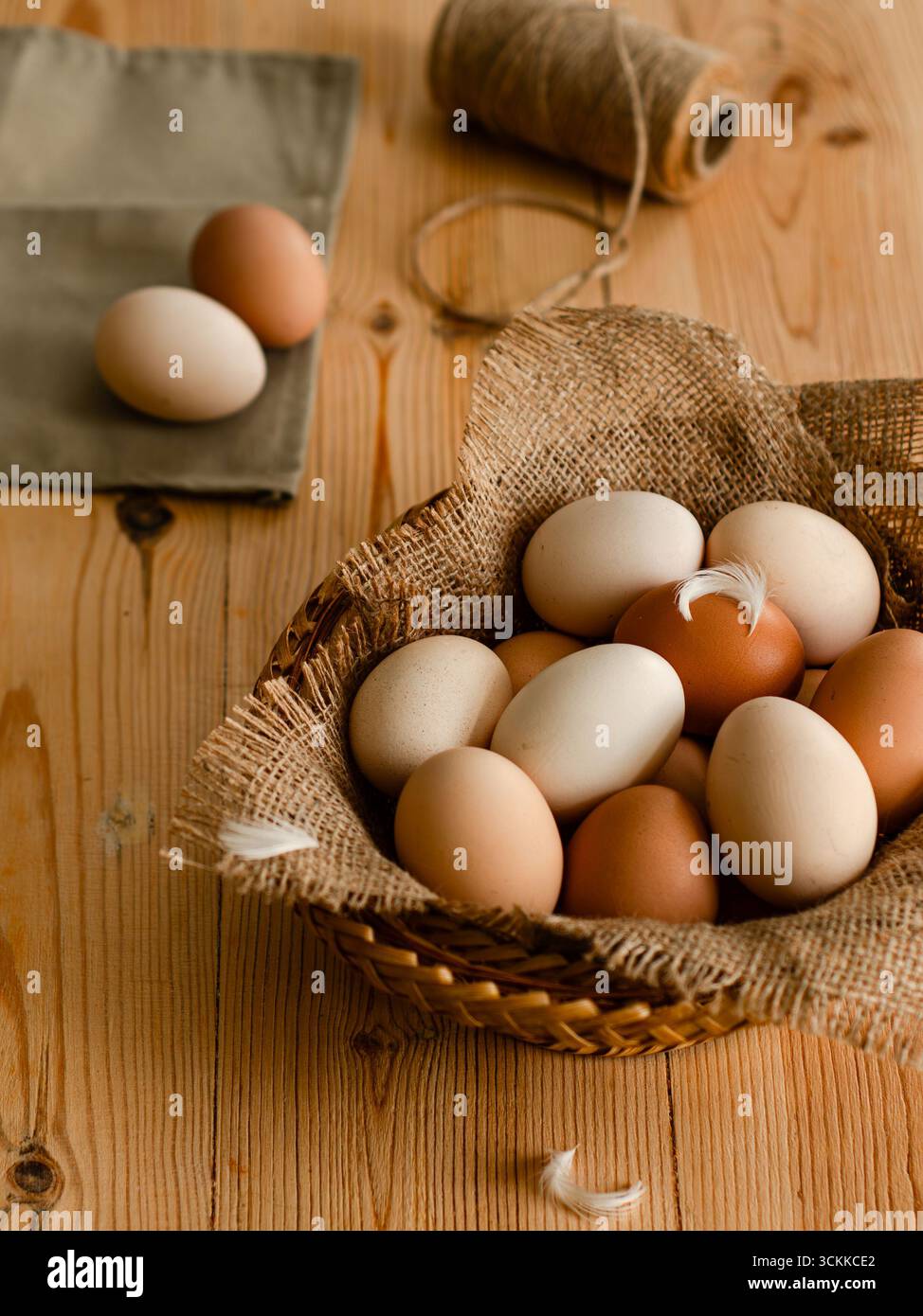 Basket of organic farm eggs on wooden table with jute sack and twine, rustic country kitchen still life. Stock Photo
