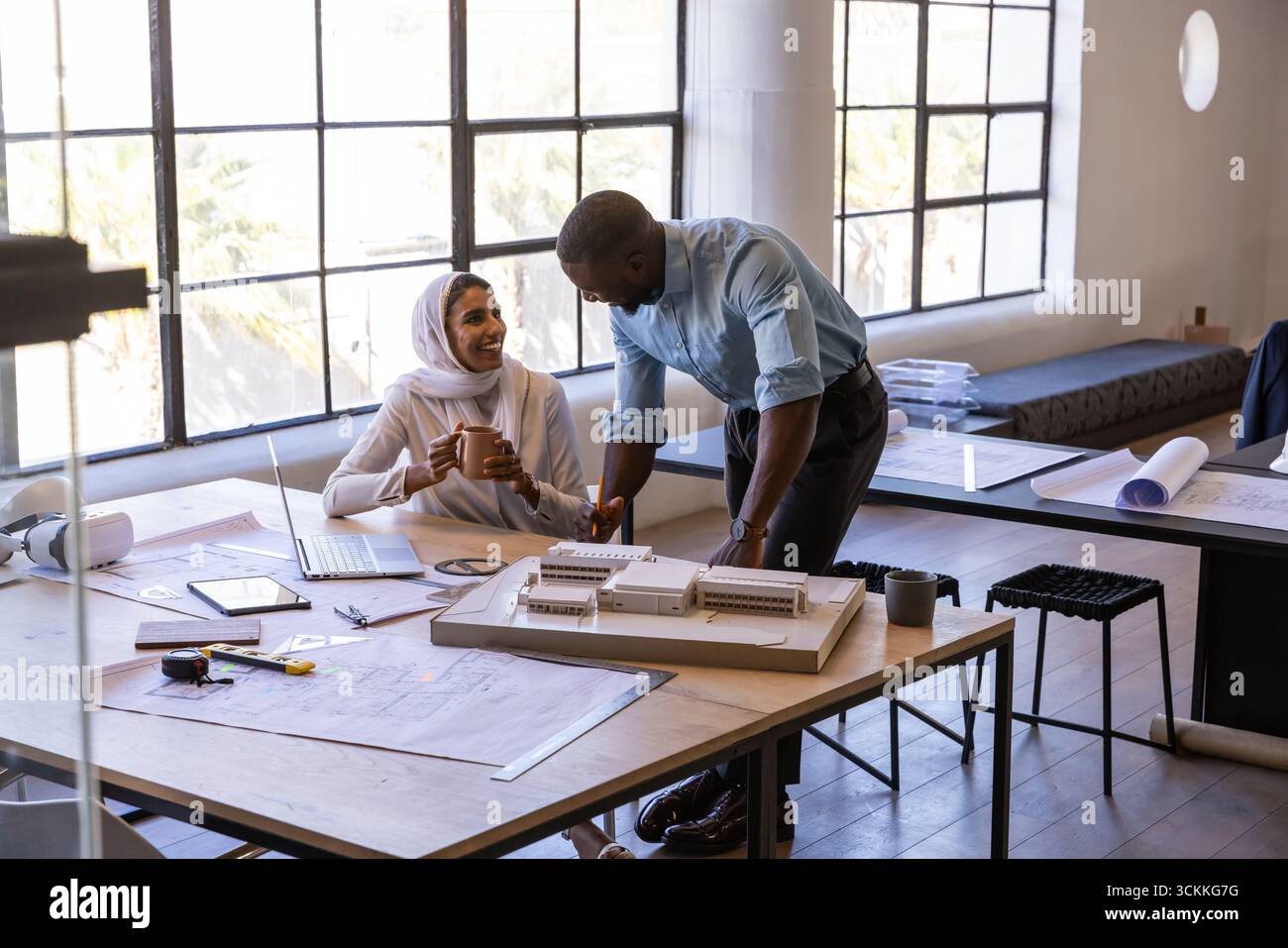 Diverse coworkers collaborating over scale model, blueprints in architecture studio with laptop Stock Photo