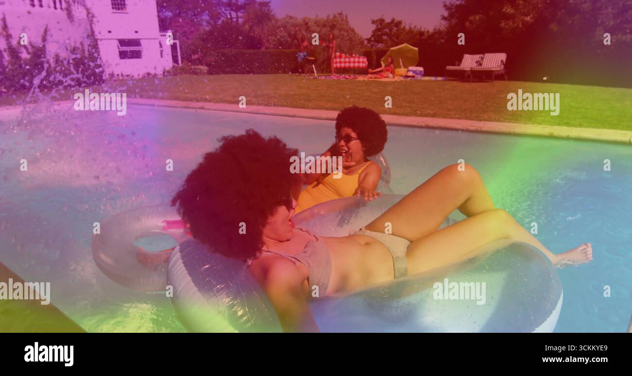 Floating two women wearing grey and yellow swimsuits in backyard pool, with rings and smartphone Stock Photo