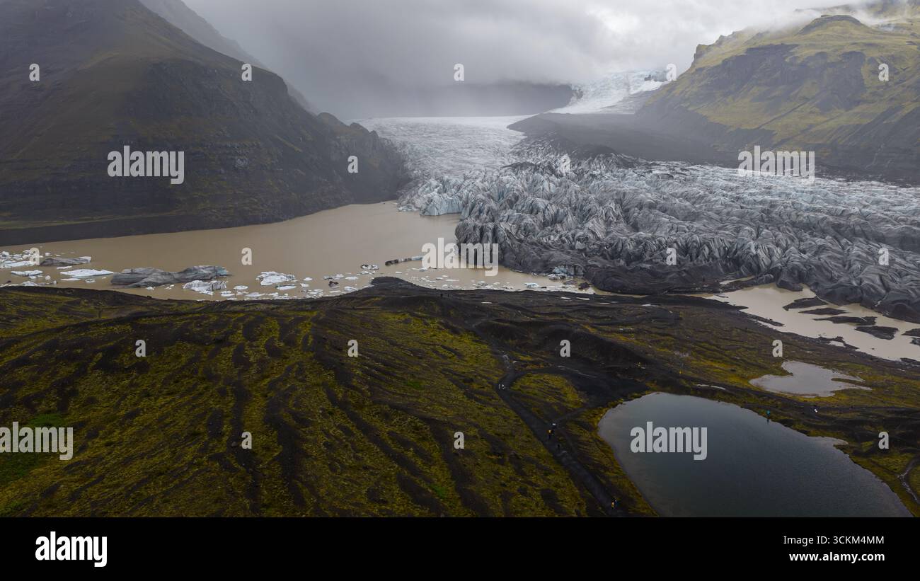A glacier in Iceland extends into a sediment filled lagoon, surrounded ...