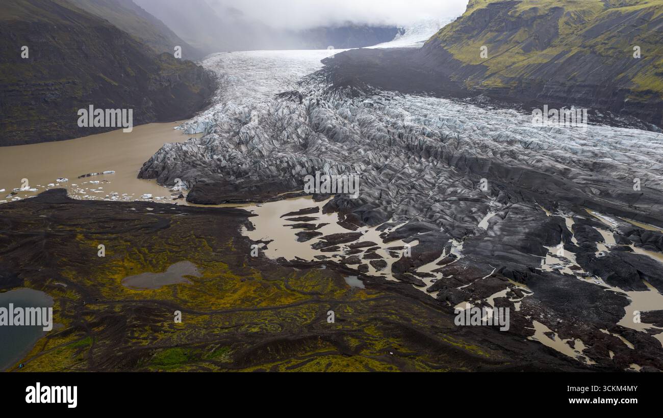 A glacier in Iceland flows into a muddy glacial lagoon, surrounded by ...