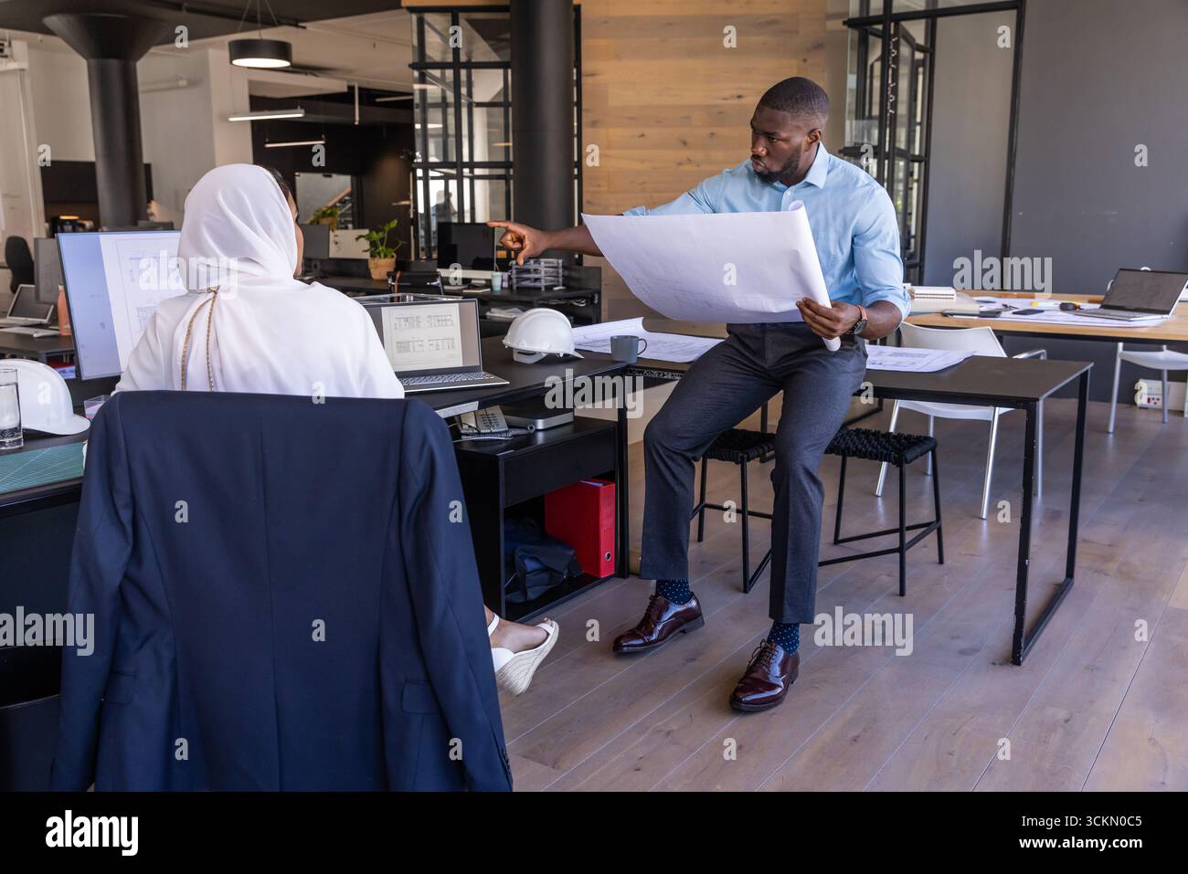 Diverse architects working on blueprint at open-plan office desk with laptop, copy space Stock Photo