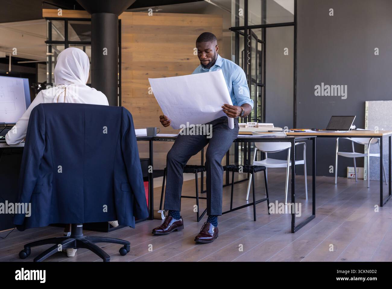 Diverse coworkers collaborating on blueprint sheet while examining computer in office Stock Photo