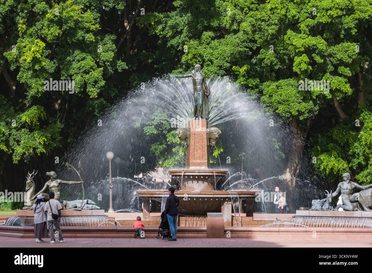 Majestic Archibald Memorial Fountain with intricate sculptures, surrounded by green trees and visitors enjoying the scene, Sydney Stock Photo