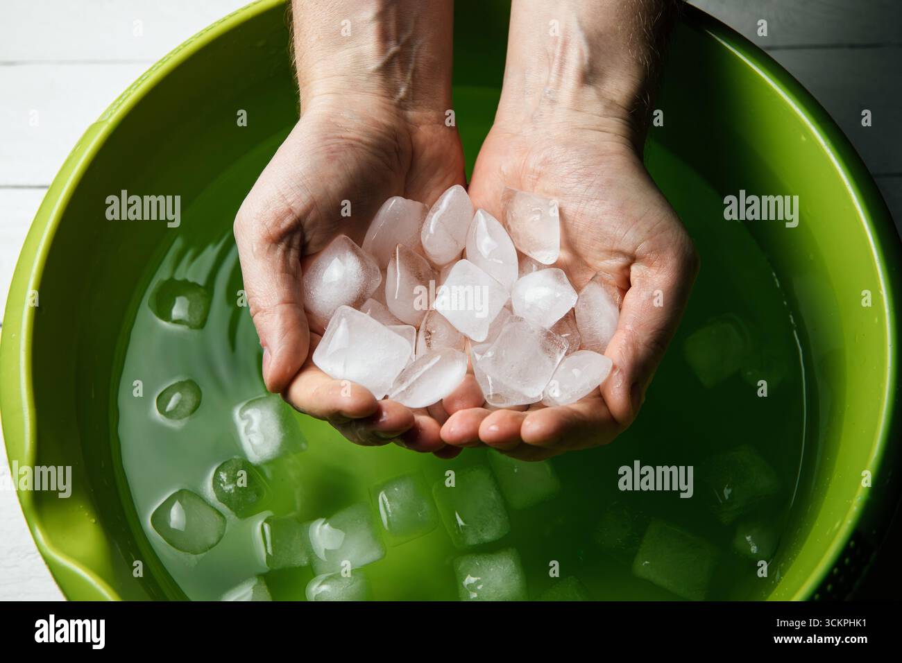 Man holding hands inside ice water bowl with ice cubes. Cold exposure ...
