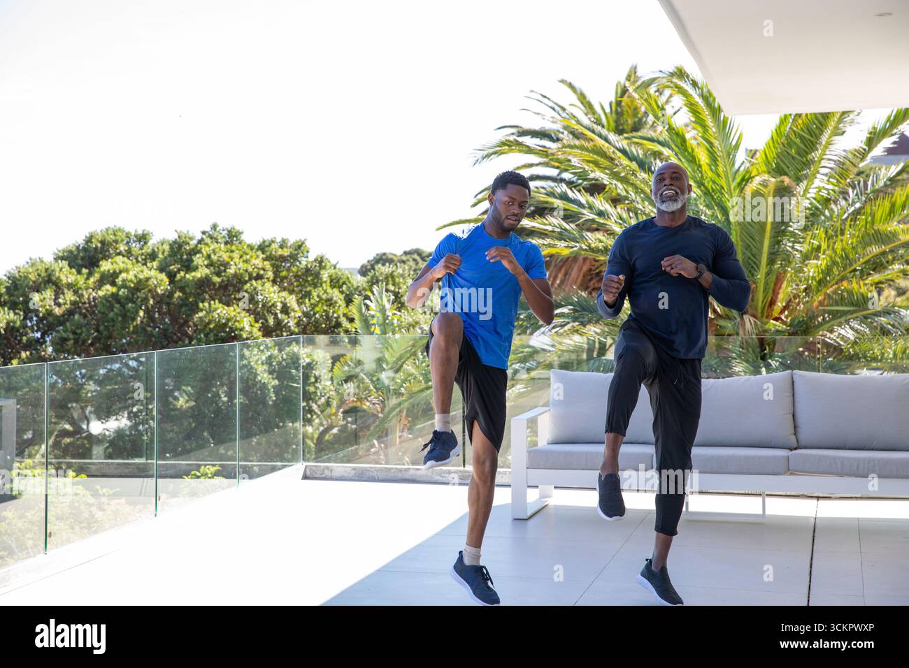 African american family doing high-knee exercise on terrace with glass ...