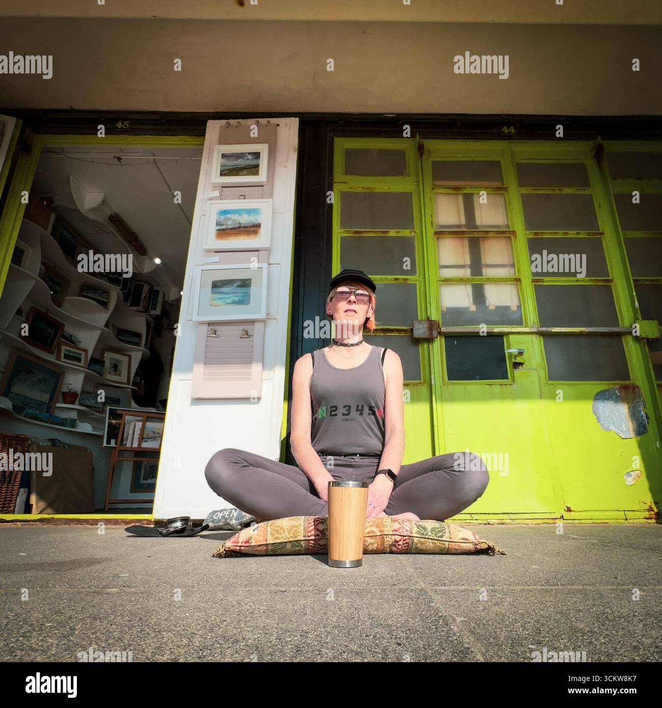 An artist sitting cross legged outside her studio looking out to sea - Smartphone Captured Stock Image
