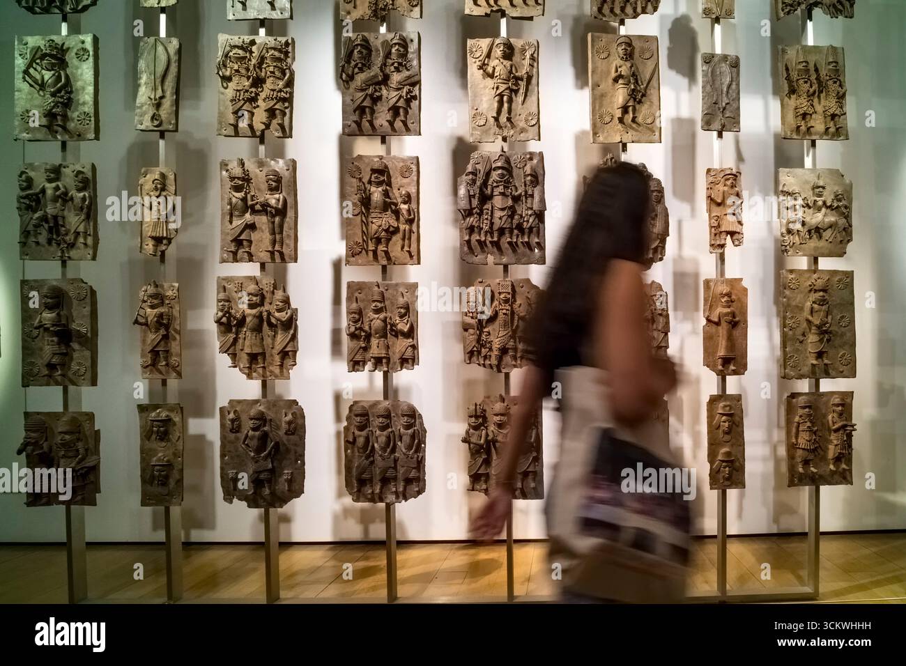 A visitor passing a display of C16th cast brass plaques from Benin, Nigeria.  On display at the British Museum. Stock Photo