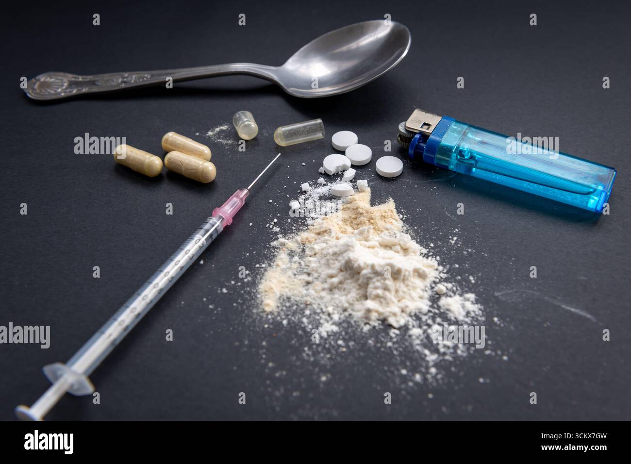 A medical syringe, a table spoon, a lighter, and crushed medical tablets mixed with white flour on a black background. An unlawful drug taking, addict Stock Photo