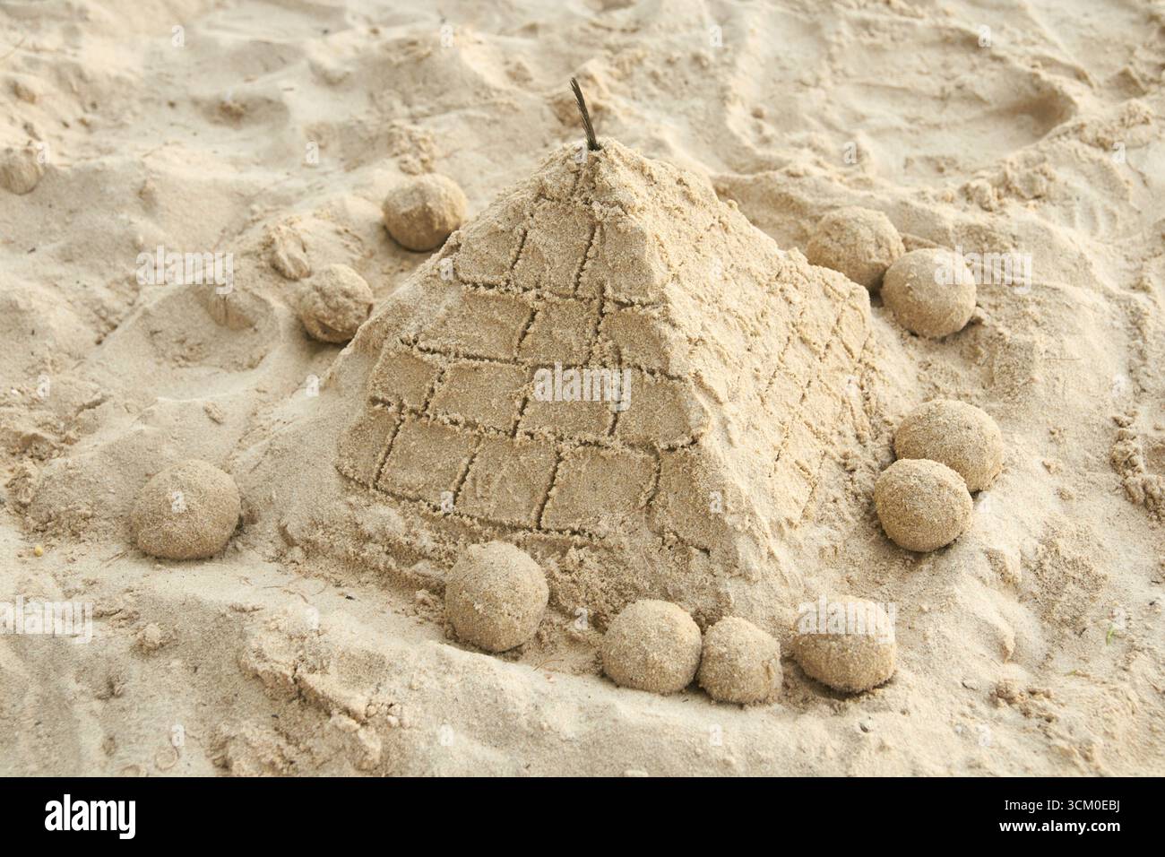 Sand pyramid on beach surrounded by spherical sand sculptures in sunlit setting. Stock Photo