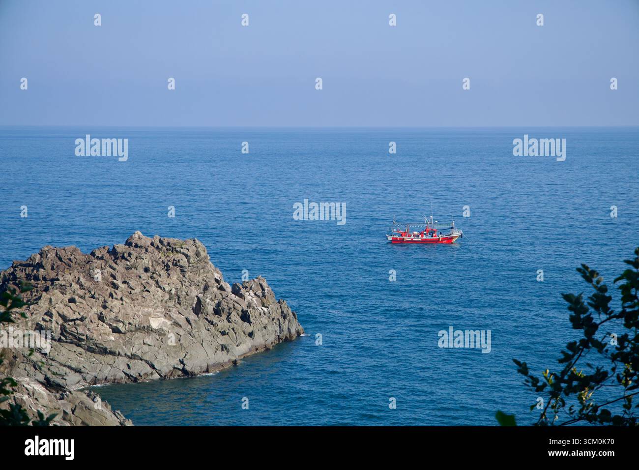 A red fishing boat sails past dark volcanic rocks near the Oedolgae ...