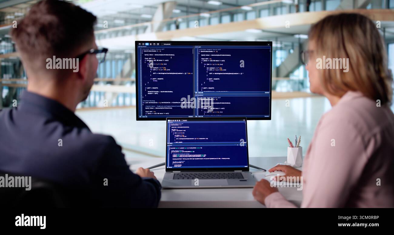 Male Developer Typing Code On Laptop With Female Trainee In Office. Stock Photo