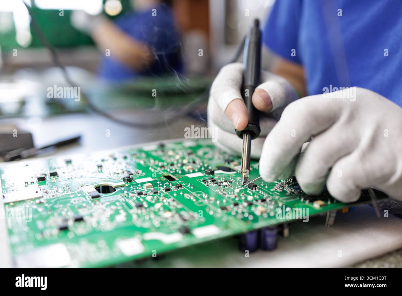 Closeup of ESD gloved worker soldering parts on a green PCB at an electronics assembly workstation in a modern factory Stock Photo