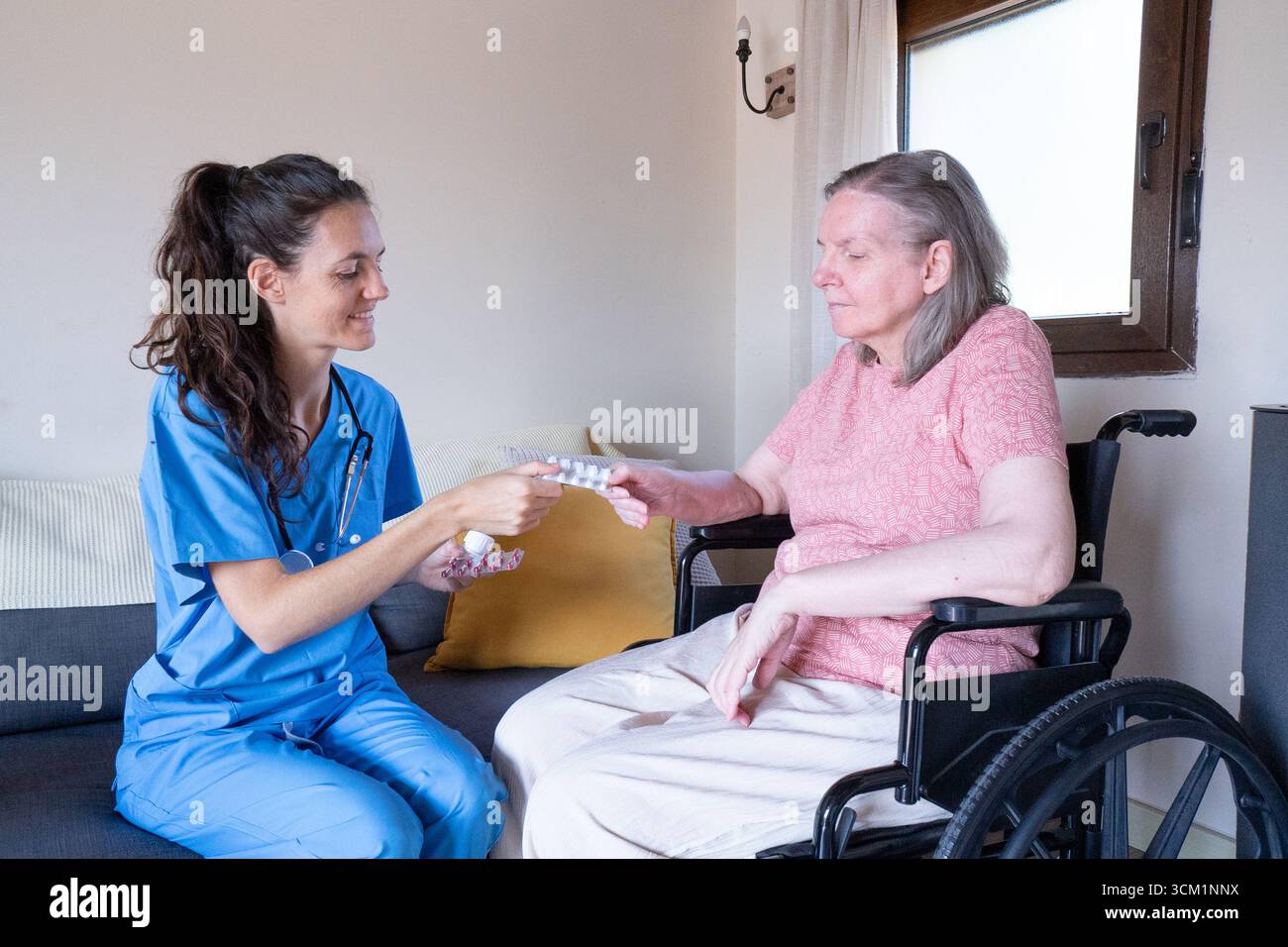 Doctor giving medicine to elderly retired woman sitting in wheelchair at home or nursing home Stock Photo