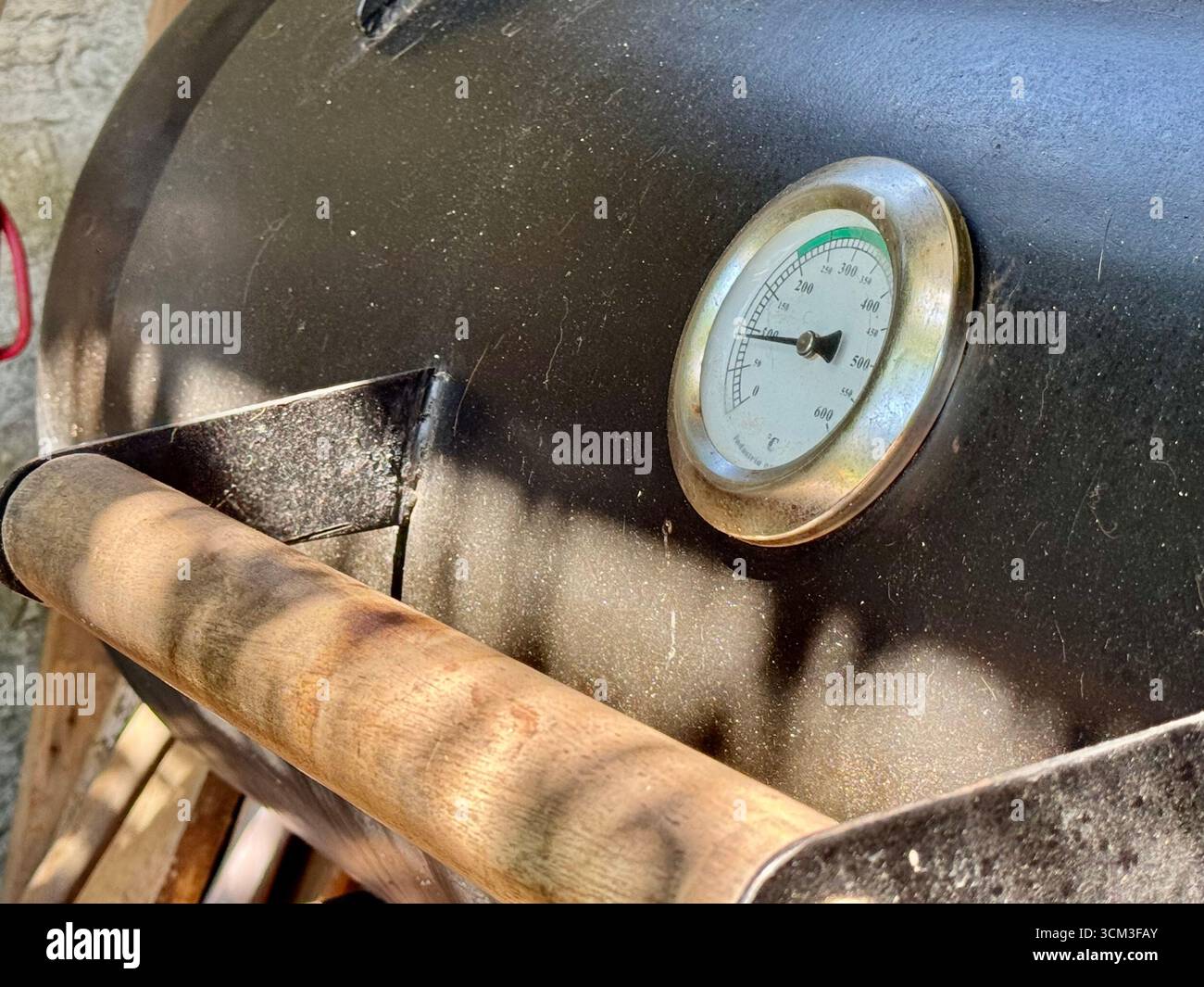 Close-up of a temperature gauge on a barbecue smoker and a person basting grilled meat on an outdoor barbecue in Buenos Aires, Argentina. - Smartphone Captured Stock Image
