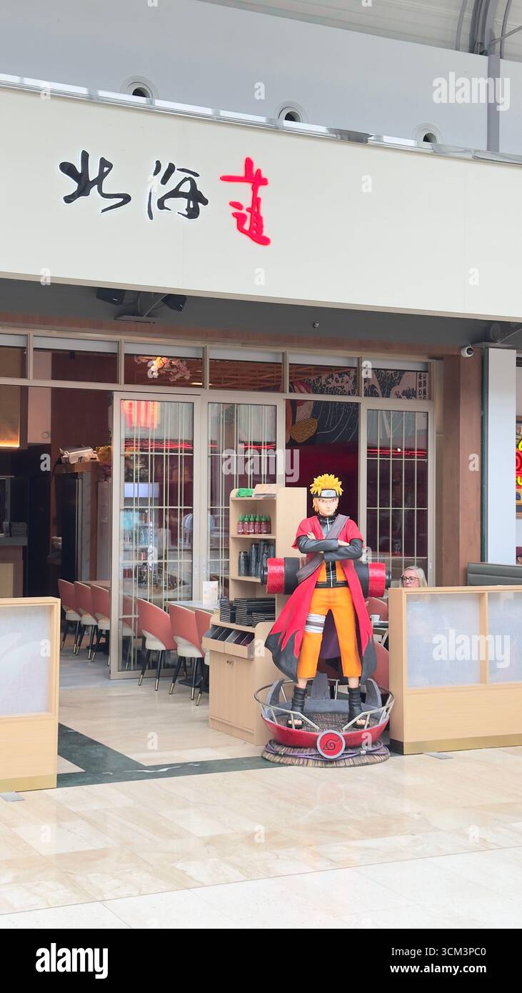 A Naruto statue stands outside a restaurant with Asian-style signage and decor. The statue is vibrant, with the restaurant interior visible through gl Stock Photo