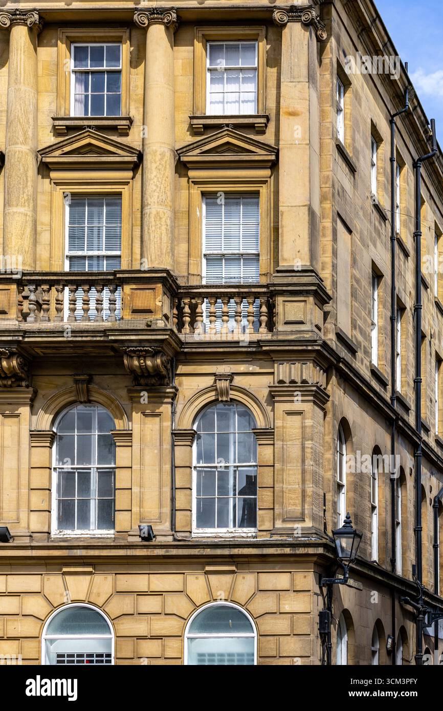 A close-up view of a tan stone building's corner facade featuring multiple windows of various shapes and sizes, a decorative balcony, and architectura Stock Photo