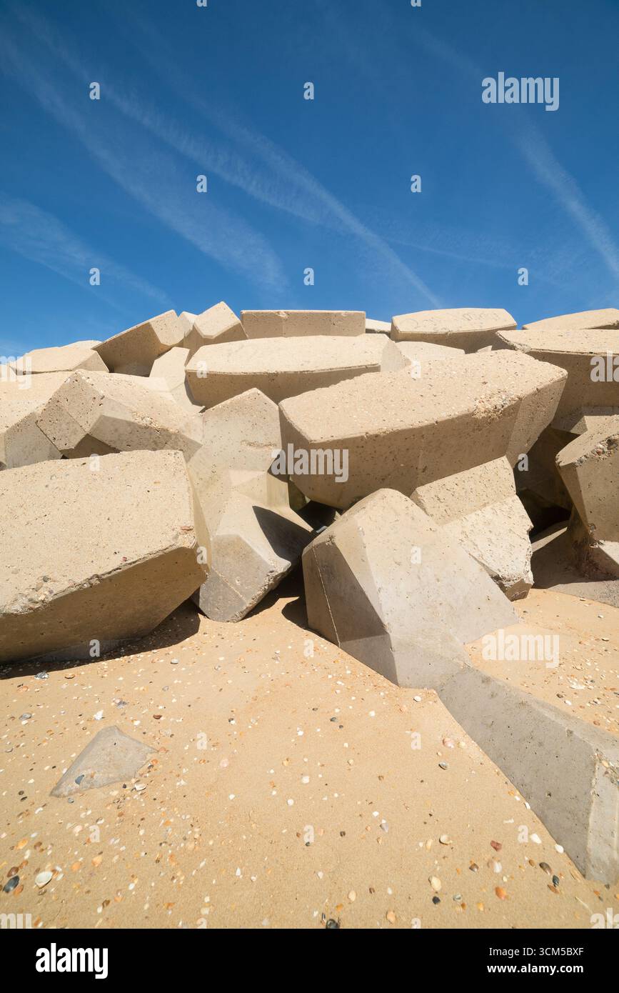 Bloques de hormigón hexagonales formando un espigón protector en la playa y puerto deportivo bajo un cielo azul claro. Hormigon armado y artificial Stock Photo