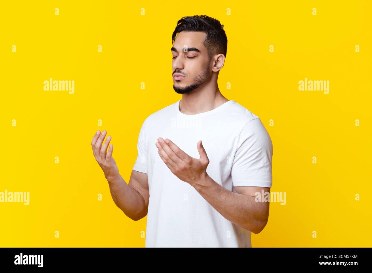 Religious young arab man praying on yellow background, copy space Stock Photo