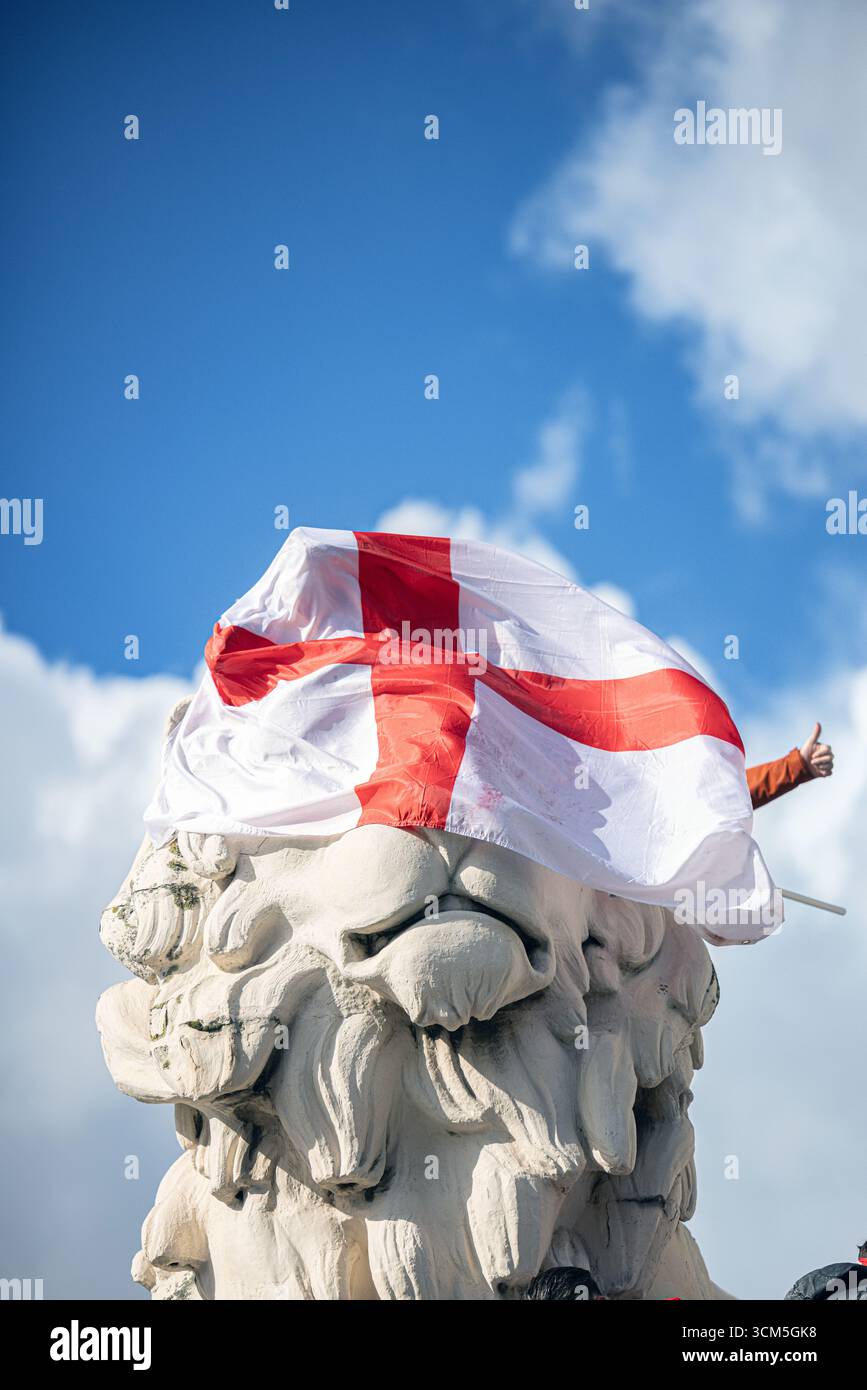 The historic South Bank Lion in London, UK, with its face partially shrouded by a St. George’s Cross flag, symbolizing English identity. Stock Photo