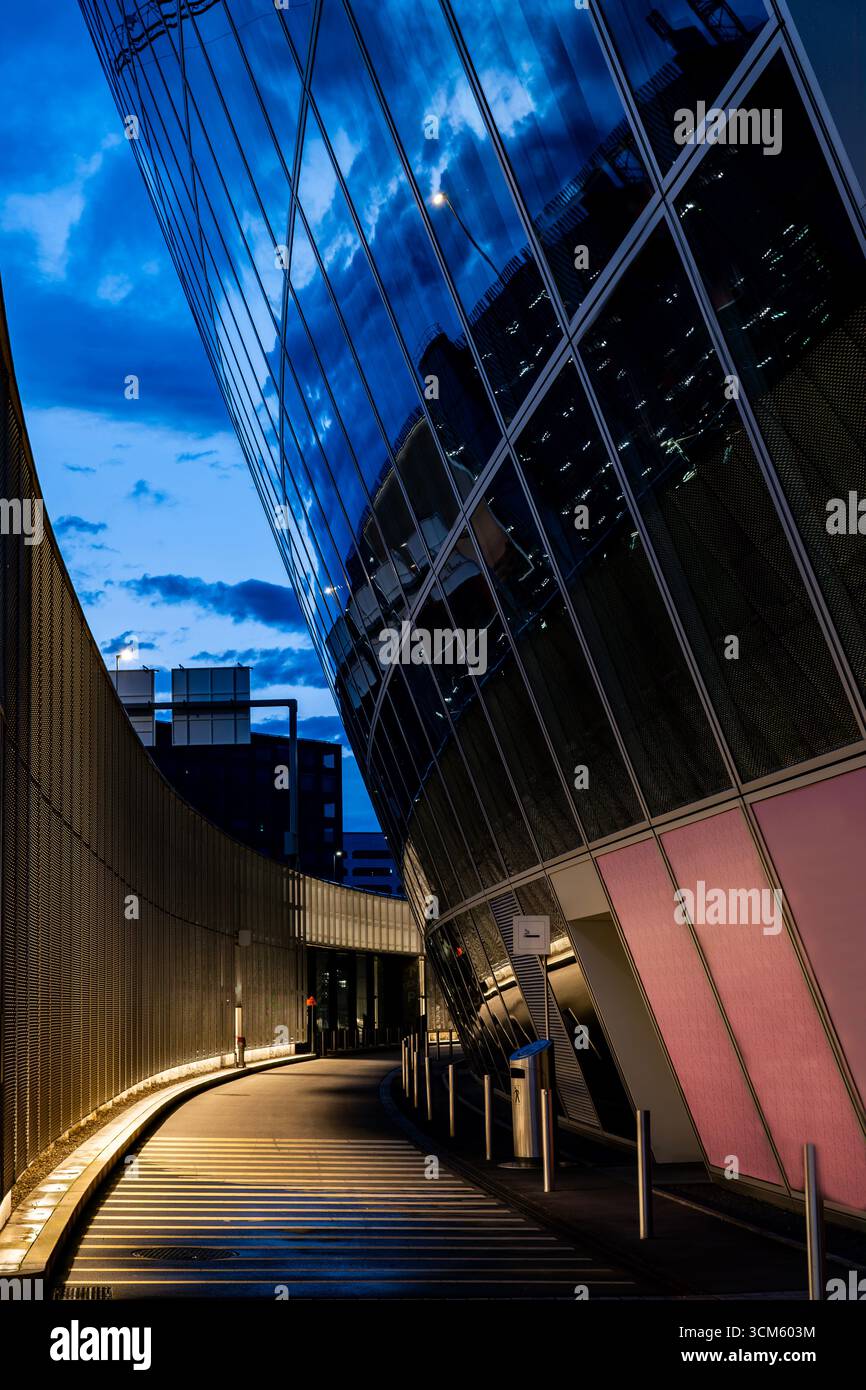 Illuminated Road with a Wall and Modern Glass Building with Reflection to Circle in Dusk in Kloten in Zurich Airport in Kloten, Zurich, Zurich Canton, Stock Photo