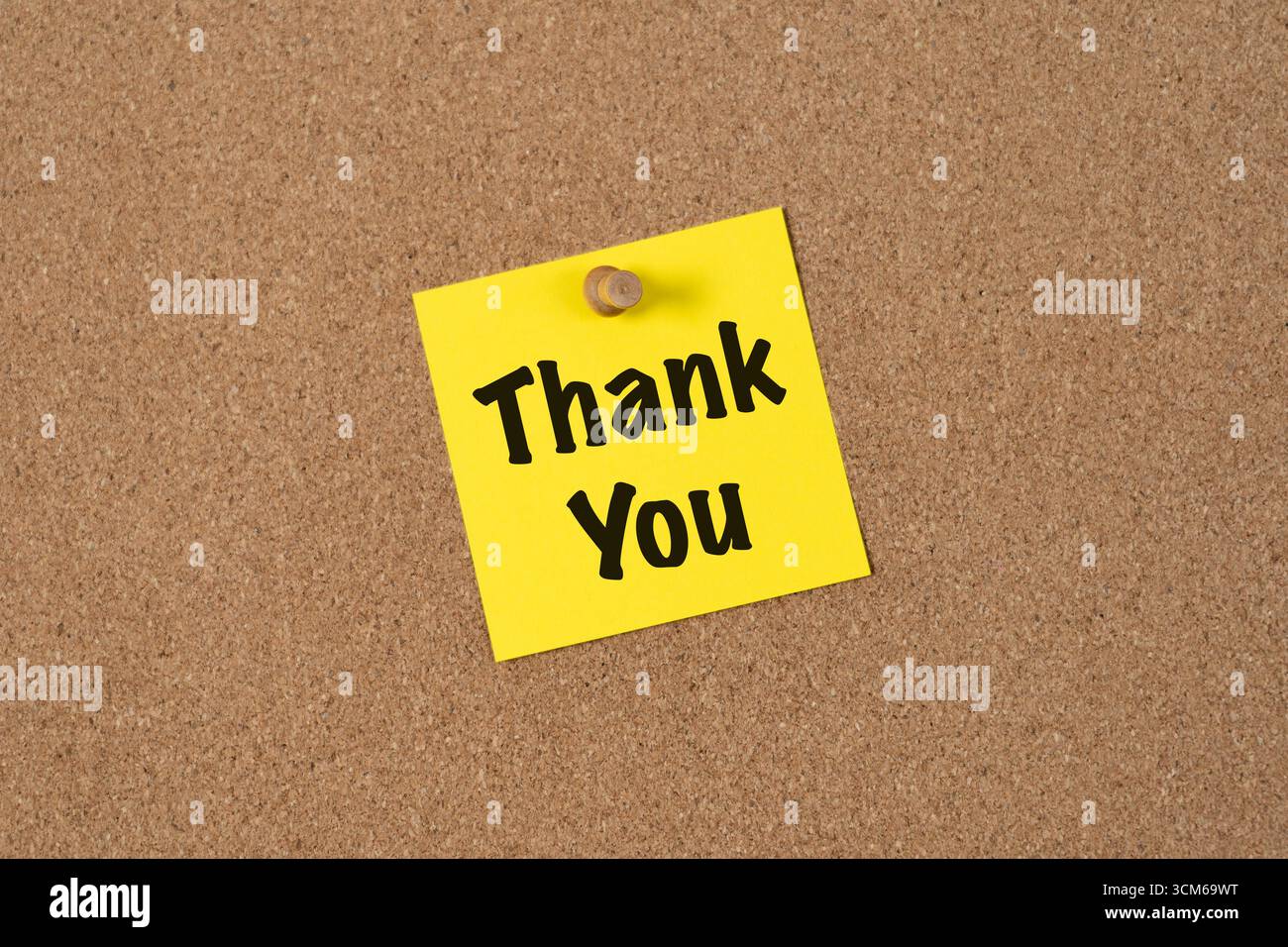 A yellow sticky note with the words Thank You in bold black text pinned to a corkboard. The note conveys gratitude and appreciation in a simple, clear Stock Photo
