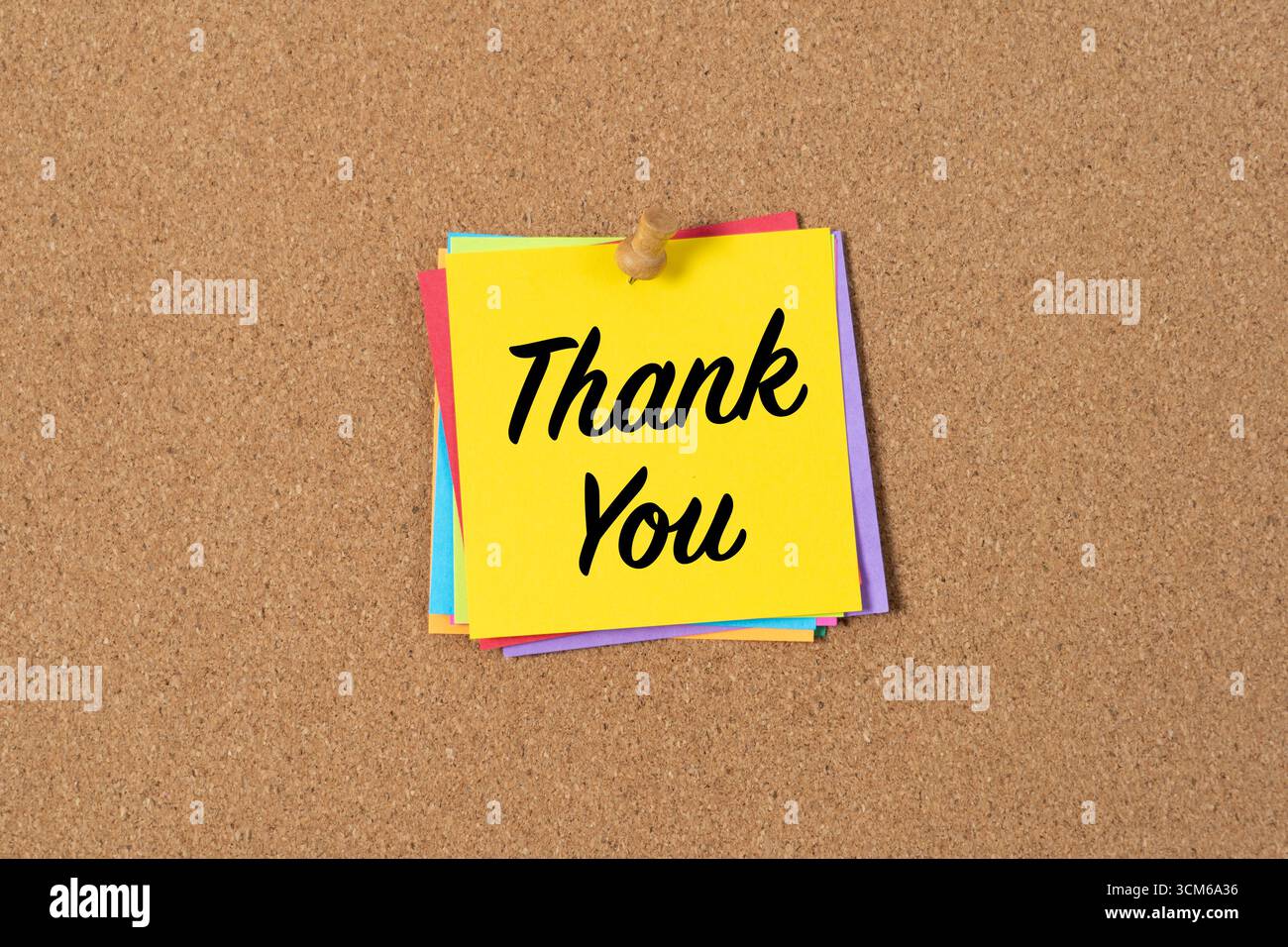 A yellow sticky note with the words Thank You in bold black text pinned to a corkboard. The note conveys gratitude and appreciation in a simple, clear, and cheerful way. Stock Photo