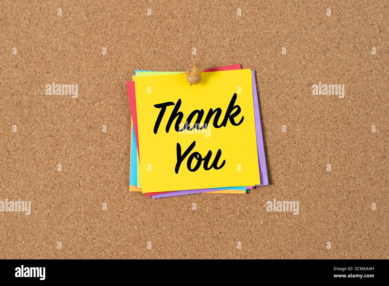A yellow sticky note with the words Thank You in bold black text pinned to a corkboard. The note conveys gratitude and appreciation in a simple, clear, and cheerful way. Stock Photo
