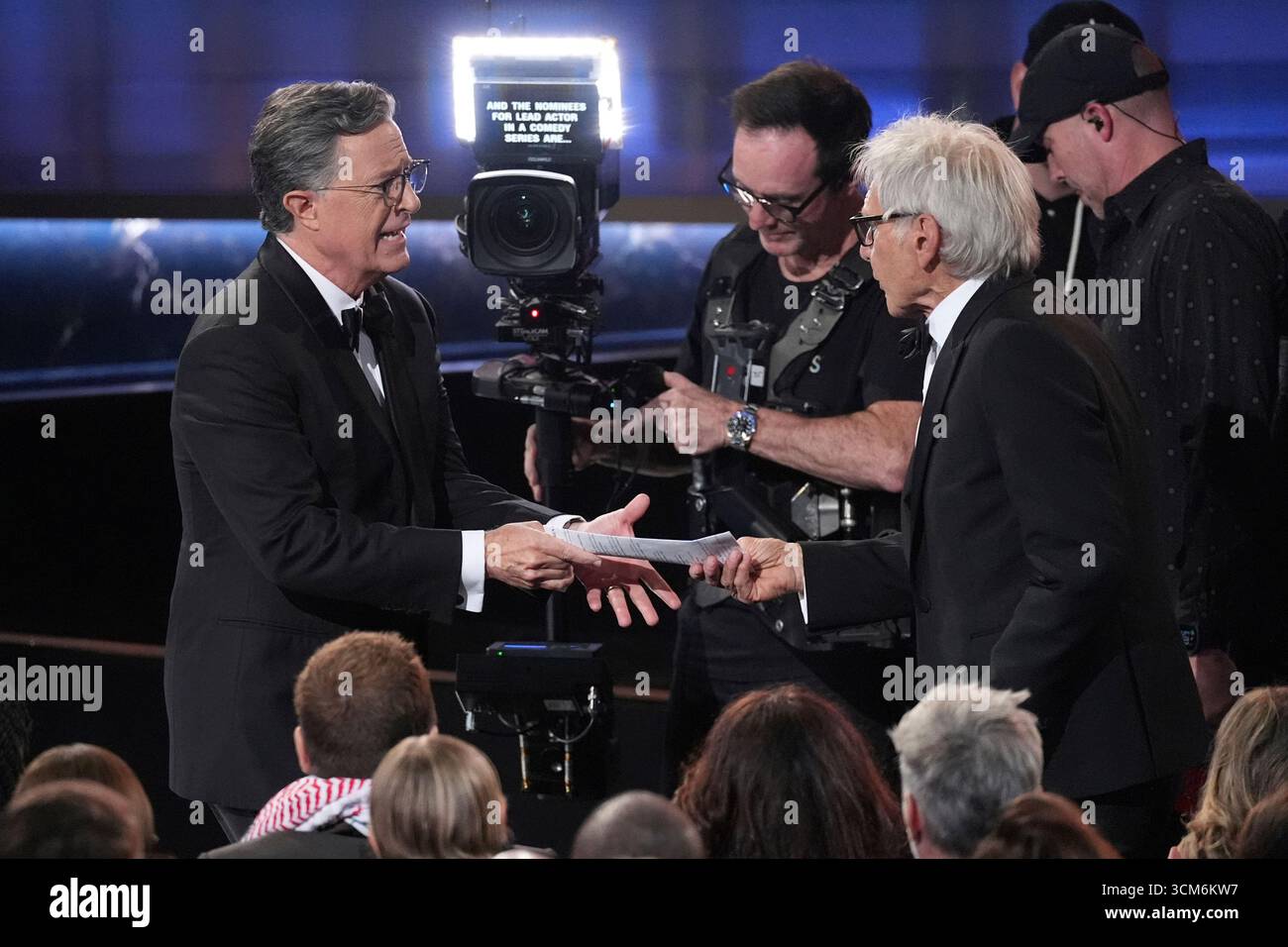 Stephen Colbert, left, hands Harrison Ford his resume during the 77th