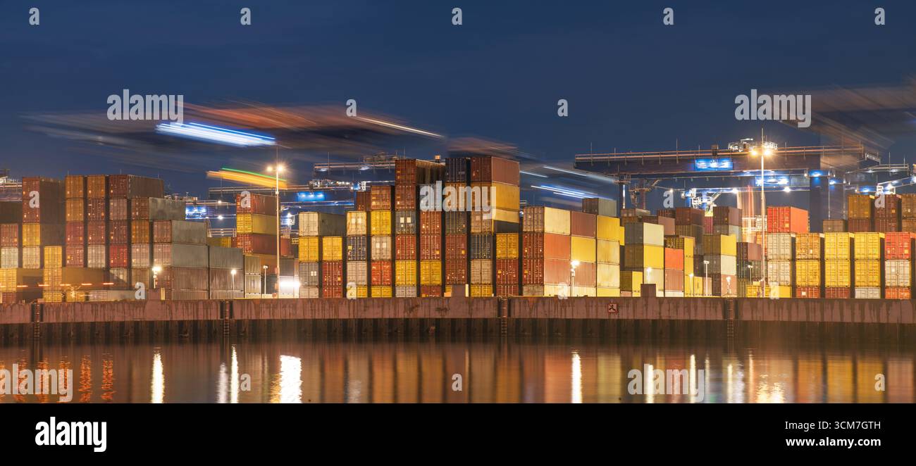 Cranes moving along a programmed trajectory above stacks of containers Stock Photo