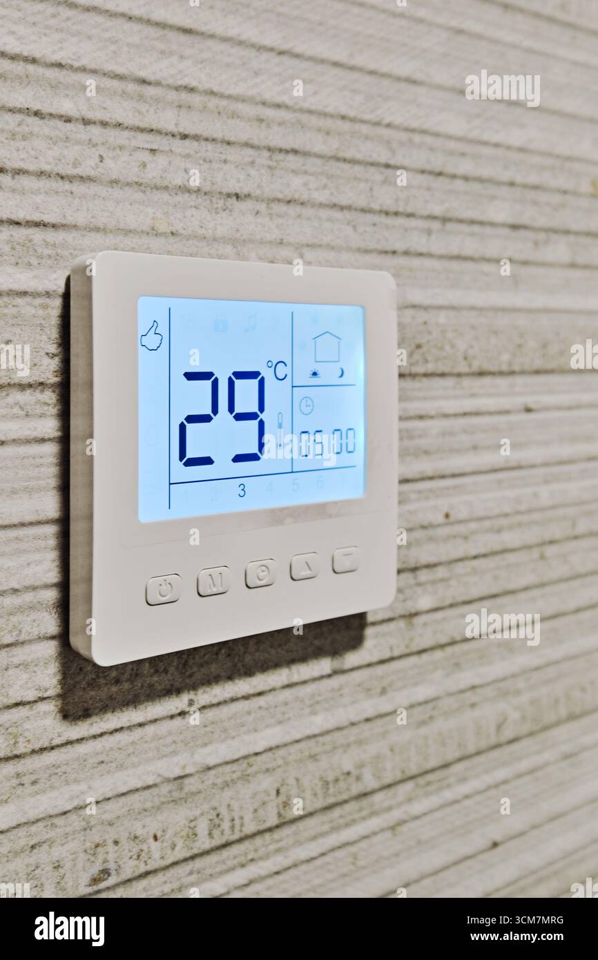 Close-up of smart digital thermostat installed on modern textured wall. Energy-efficient climate control, smart home systems, automated heating and co Stock Photo