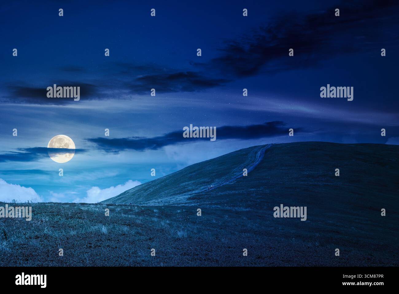 path for mountain tourism in summer at night. alpine landscape. beautiful scenery of ridge with green hills under blue sky with clouds in full moon li Stock Photo