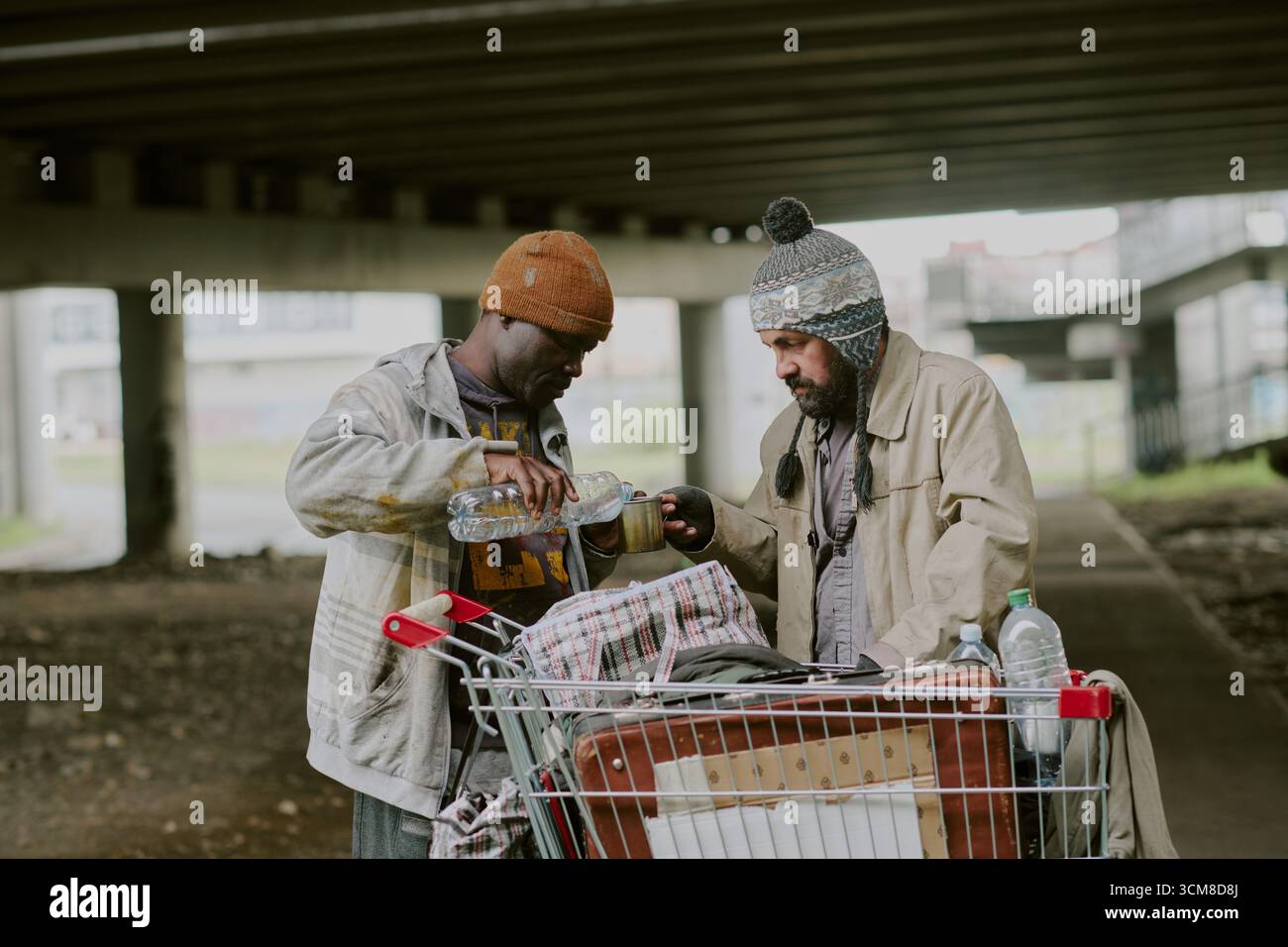 Homeless Black Man Pouring Water for Homeless Caucasian Man Outdoors Stock Photo