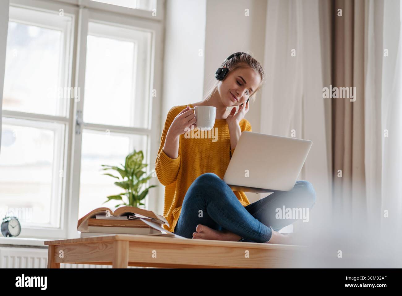 Young female student sitting at the table, using headphones while studying. Stock Photo