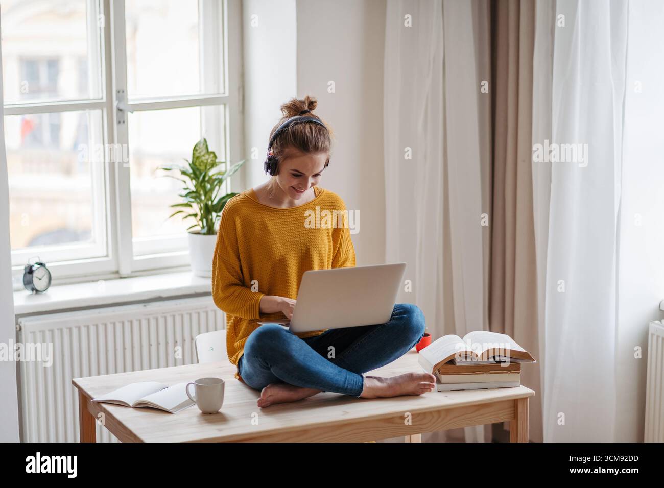 Young female student sitting at the table, using headphones while studying. Stock Photo