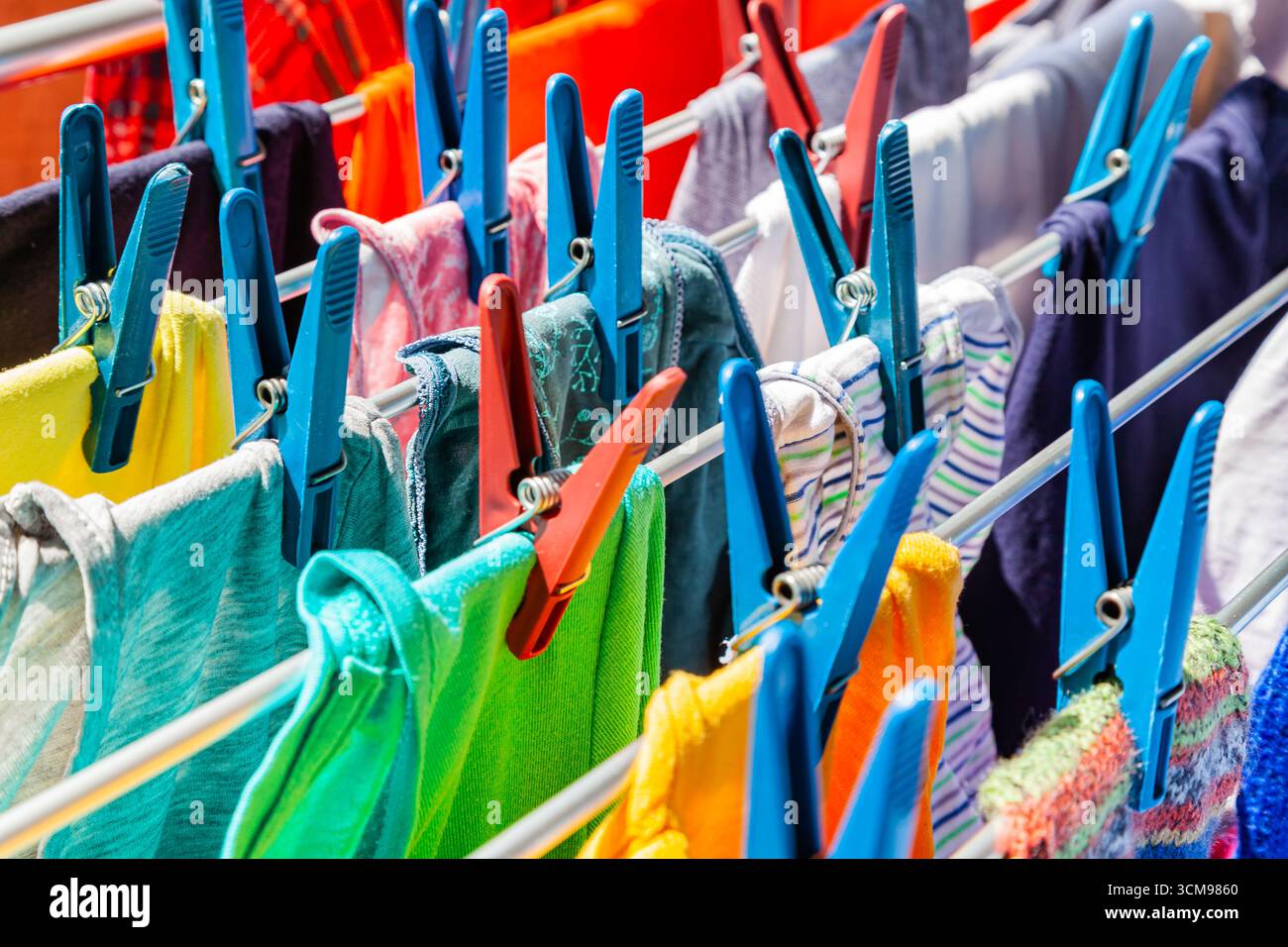 Multi-colored clothes hang attached to clothespins and dry after washing, close-up. Stock Photo