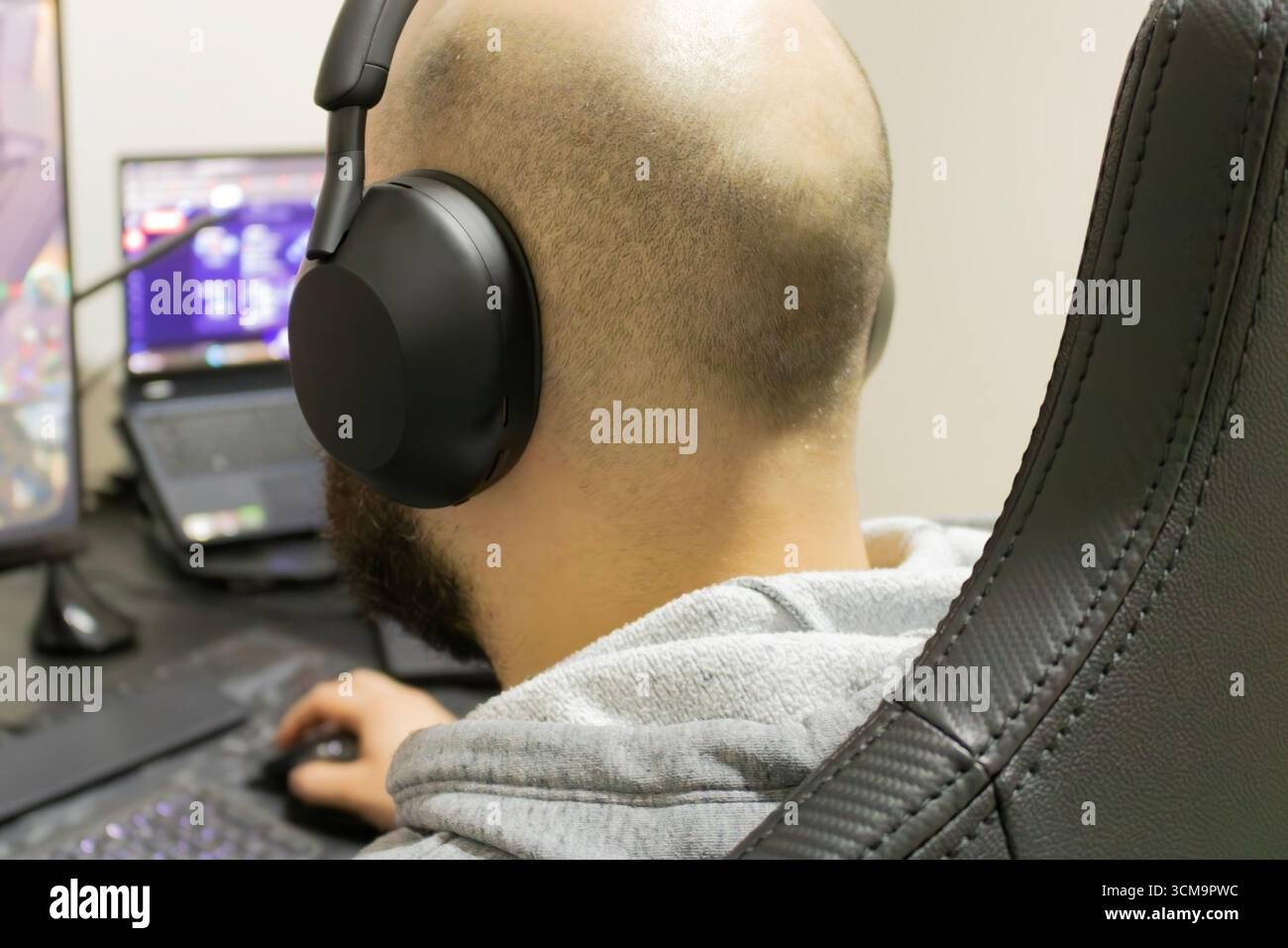 Man playing a computer game with headset, seen from behind. Desk with two monitors Stock Photo