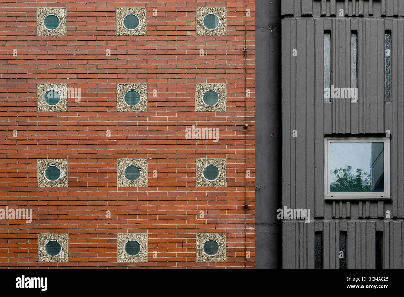 Architectural Contrast: Dual Textures and Patterns. At RWTH Aachen University in Germany, a facade contrasts red brick with circular windows and grey panels with rectangular forms, blending traditional and industrial elements into a striking composition. Stock Photo