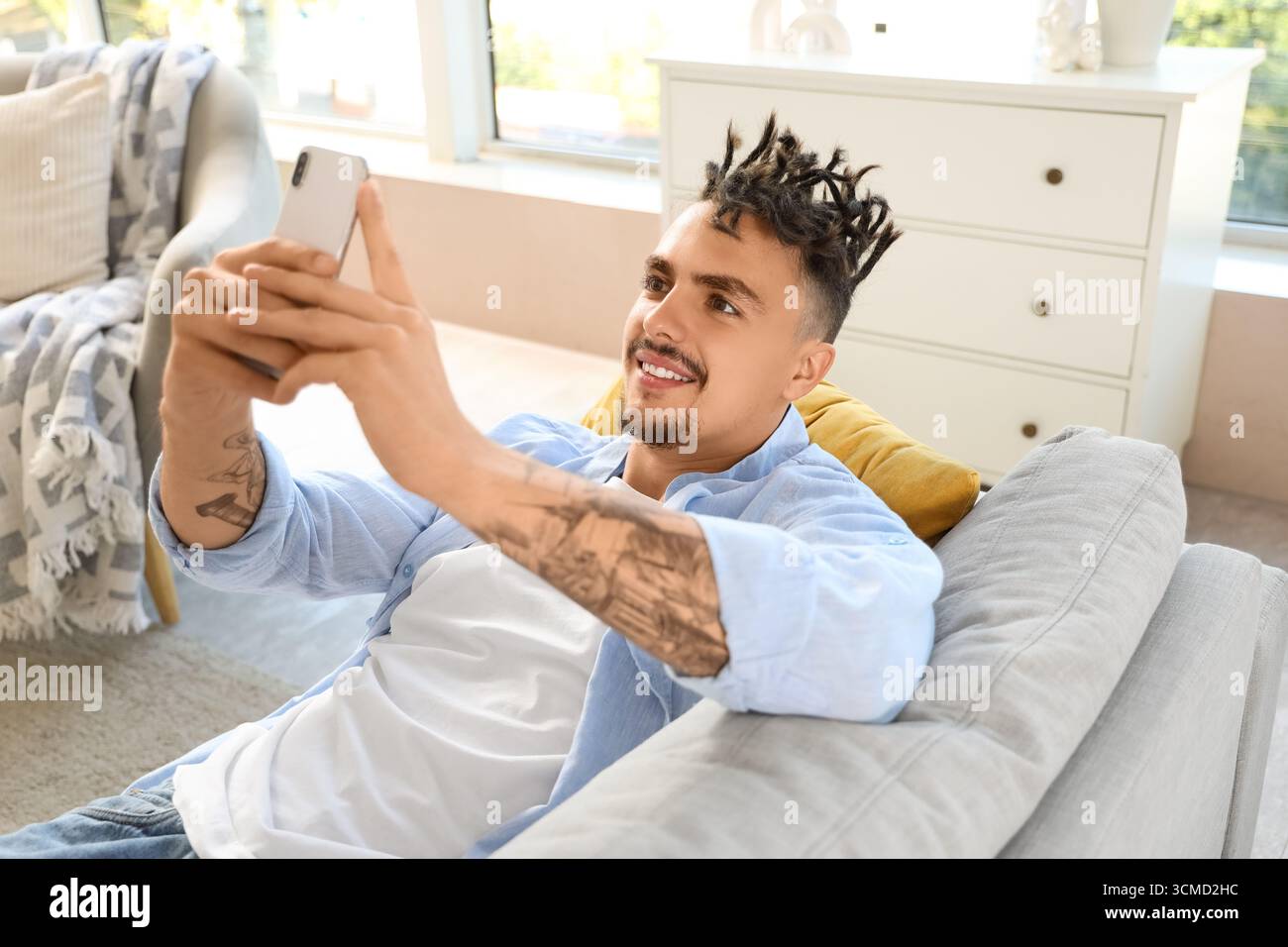 Young man with dreadlocks using mobile phone on sofa at home Stock Photo