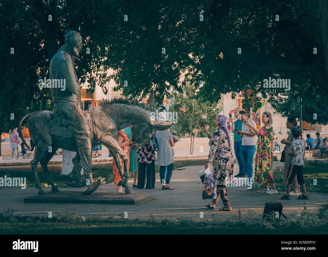Group of Uzbek people including adults, women, men, and kids gather around Hodja Nasreddin statue in Bukhara, Uzbekistan. Stock Photo