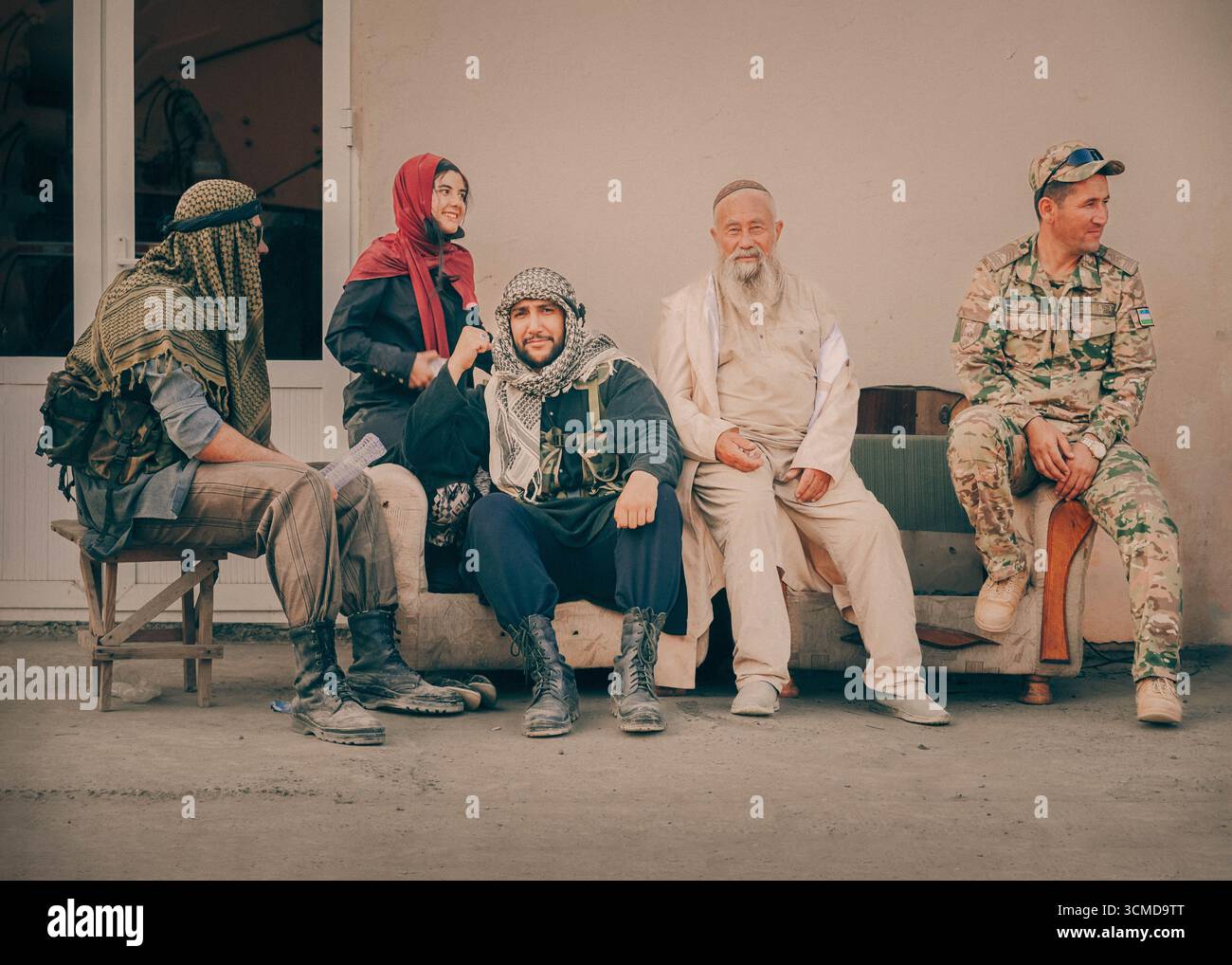 Men and women in diverse traditional attire, sitting and posing outside a building in Bukhara, Uzbekistan, expressing camaraderie and cultural fusion. Stock Photo
