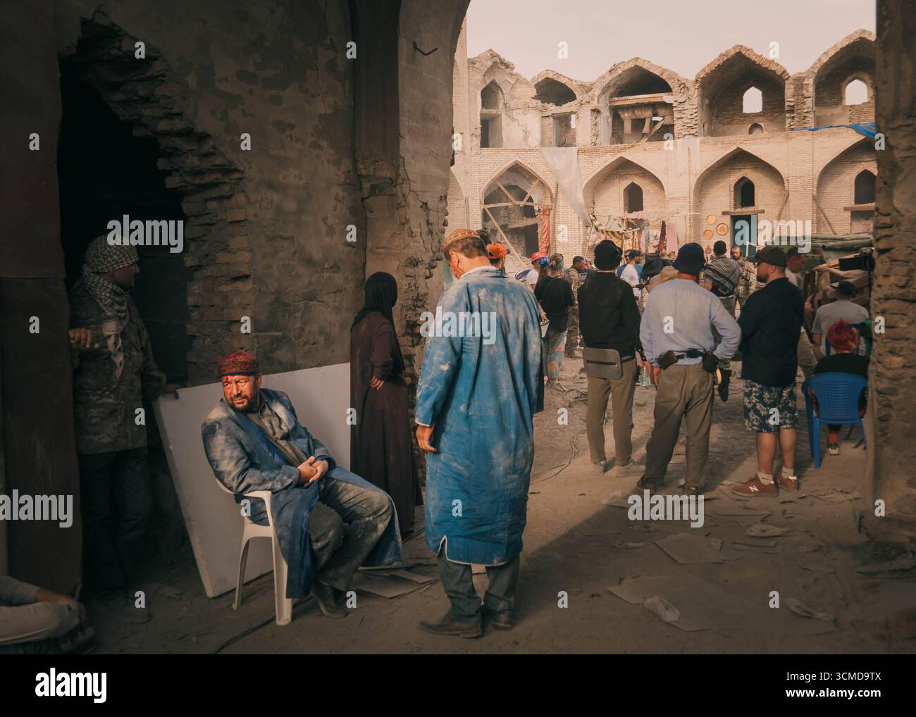 Men and a woman dressed in traditional and modern attire, gathering and interacting in a historic, weathered courtyard in Bukhara, Uzbekistan. Stock Photo