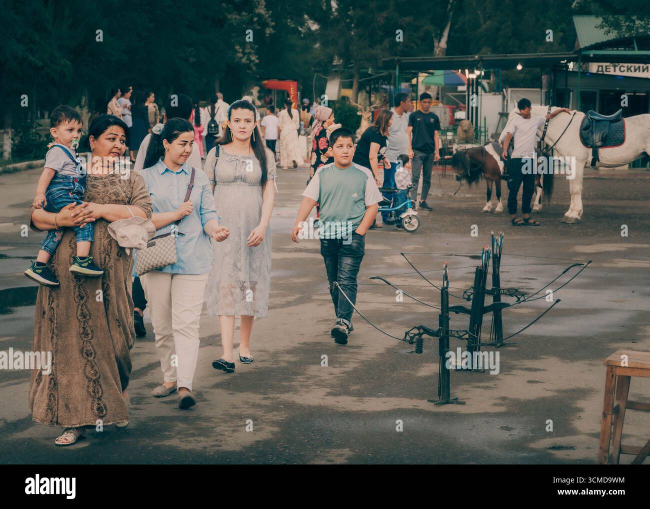 Family group walks in Bukhara, Uzbekistan, with mother carrying toddler and teens observing surroundings. Stock Photo