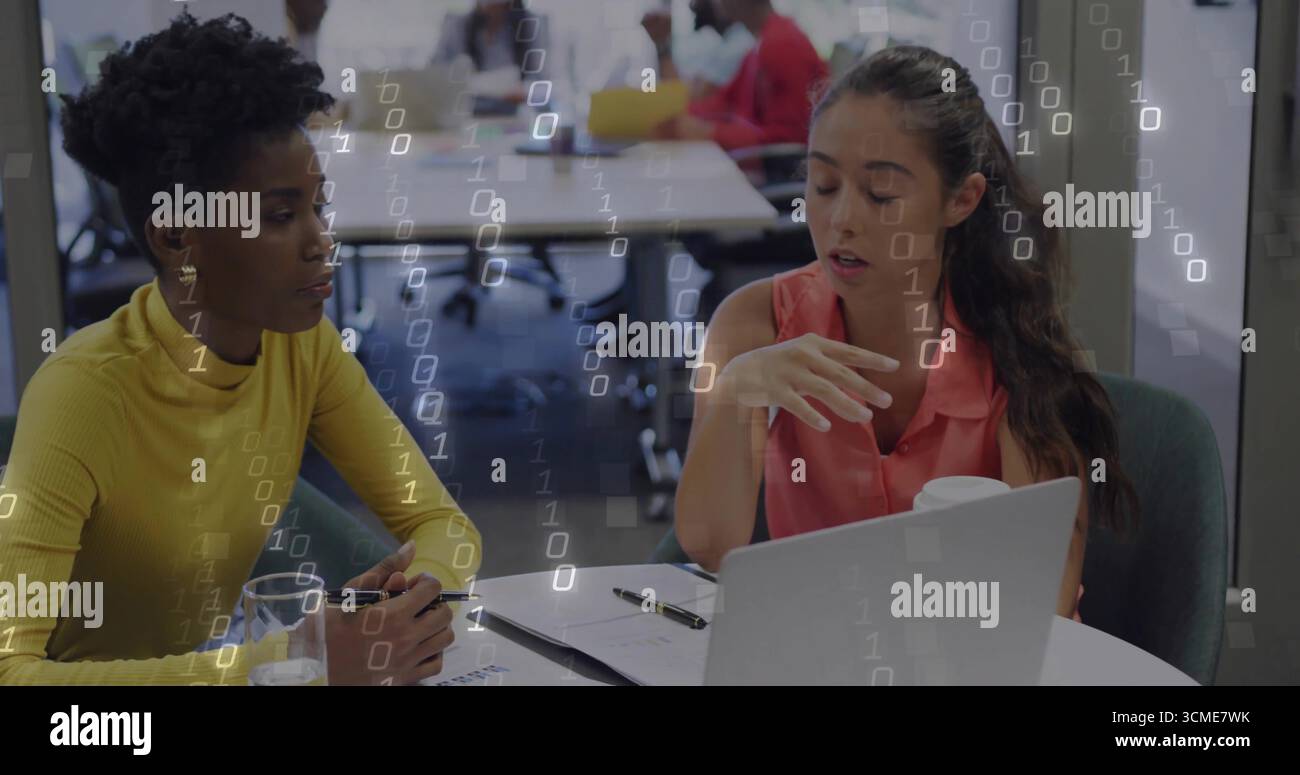 Discussing project details women sitting at table in open-plan office with laptop and documents Stock Photo