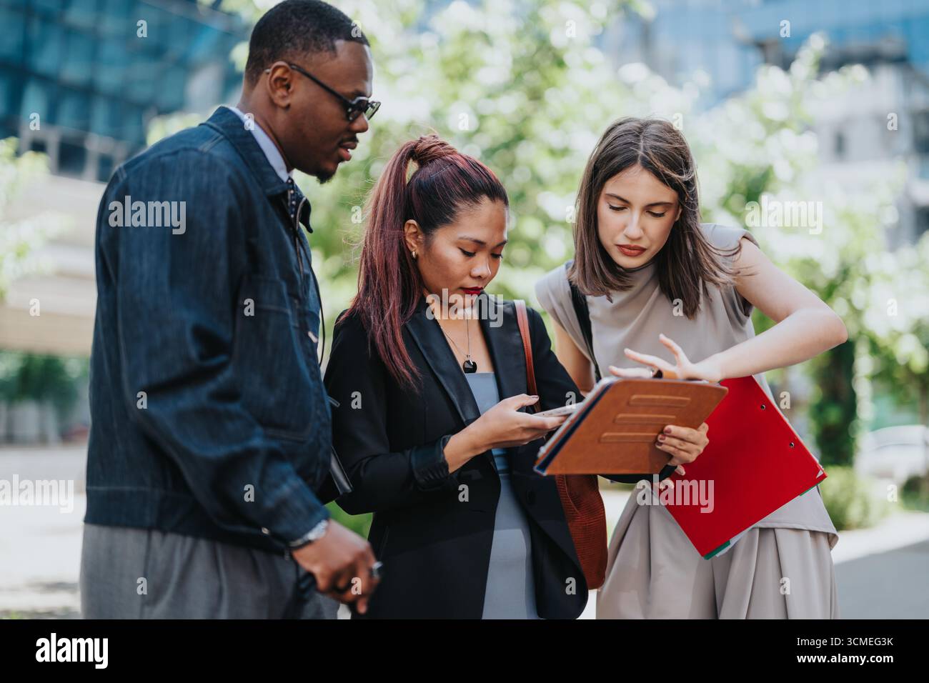 Multiracial colleagues collaborating outdoors with documents and a digital device Stock Photo